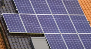 Techniker montiert Solarmodule auf Schrägdach mit Stromspeicher im Hintergrund